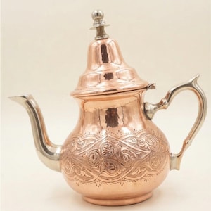 Peut inclure: Une théière en cuivre avec une finition polie, une anse argentée, un bec verseur argenté assorti et un couvercle amovible surmonté d'un bouton argenté. Le corps de la théière est orné d'un motif floral complexe en relief.