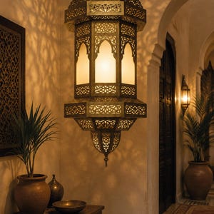 May include: A hanging pendant lantern crafted from antique brass metal with intricate laser-cut geometric patterns and frosted glass panels. The lantern emits a warm, soft glow, casting detailed shadows on the surrounding walls and ceiling.
