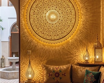 May include: A large circular wall-mounted light fixture with an intricate golden filigree pattern that casts a radial glow. The fixture is centered on a warm-toned wall above a sofa, accompanied by smaller metallic lamps and a patterned coffee table.