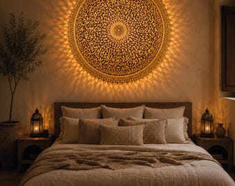 May include: A large, circular, gold-toned wall light fixture featuring an intricate, perforated mandala pattern that casts a radiant, sunburst-like glow onto the wall. The light is mounted above a bed with neutral-colored bedding and pillows.