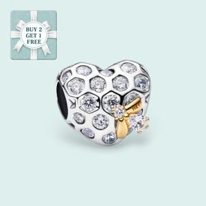 May include: A silver heart-shaped charm with a honeycomb design filled with clear crystals. A gold-colored bee with crystal accents is attached to the charm. The charm is a jewelry item.