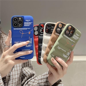 May include: A selection of colourful phone cases, including blue, red, black, white, brown, and green. Each case displays the text "DC" and "AIR", alongside other text and design features. The cases are held in someone's hands.