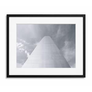 May include: Black framed print featuring a grayscale photograph of a tall, architectural structure against a cloudy sky. The structure has a triangular shape, with a bright, reflective surface. The print is matted with a white border.