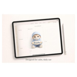 May include: A digital planner displayed on a tablet, featuring a small doll wearing a face mask and holding a sign that says "Breathe." The doll is dressed in blue and white. A stylus is next to the tablet. The text "Designed for calm, daily use" is at the bottom.