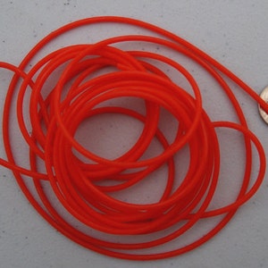 May include: A coil of bright orange elastic cord, approximately 6 mm in diameter, next to a UK 20 pence coin for scale.