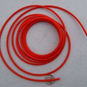 May include: A bright orange cord coiled in a circle on a white surface. A UK 20 pence coin is placed next to the cord for scale.