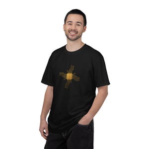 May include: Black t-shirt featuring a gold and brown graphic design. The design is a stylized cross with a central square and circuit board-like lines extending outwards. The shirt is made of a soft material.