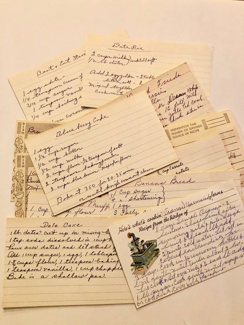 May include: A collection of vintage recipe cards with handwritten instructions for baking blueberry cake, banana bread, date pie, and date cake. The cards are yellowed with age and have a rustic, charming aesthetic.