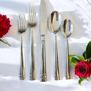 May include: A five-piece stainless steel flatware set consisting of a small fork, a large fork, a dinner knife, a large spoon, and a small spoon, all featuring a polished finish and three horizontal bands near the base of each handle.