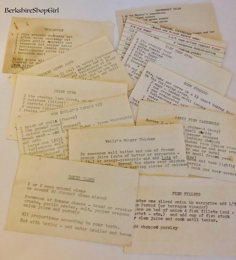 Op de afbeelding: Een verzameling vintage receptkaarten met handgeschreven instructies voor verschillende gerechten, waaronder guacamole, Ierse stoofschotel, maispudding en gebakken mosselen. De kaarten zijn verkleurd door de tijd en hebben een rustieke charme.