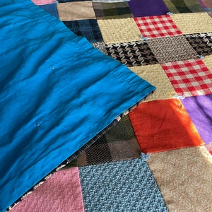 May include: A patchwork quilt with a variety of fabric squares in various colors and patterns, including plaid, houndstooth, and solid colors. A section of bright blue fabric is draped over the quilt.