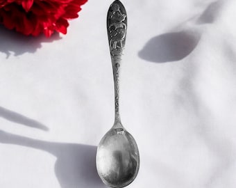 Könnte beinhalten: Ein silberfarbener Metalllöffel mit einer geprägten Mickey-Mouse-Figur am oberen Ende des Stiels. Der Stiel enthält den vertikal eingravierten Schriftzug MICKEY MOUSE in Großbuchstaben, der zu einer glatten, runden und polierten Laffe führt.