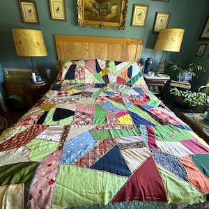 May include: A handmade crazy quilt featuring an intricate patchwork of various fabric scraps in diverse colors, patterns, and textures, including plaid, floral, and polka dot prints, all joined together with decorative embroidery stitching.