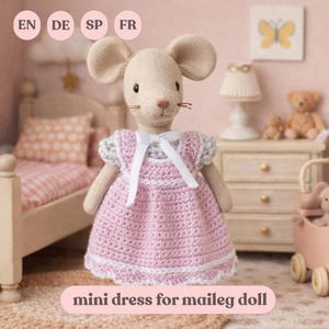 May include: A stuffed mouse doll wearing a pink crocheted mini dress with white trim and a white bow. The doll has large ears and a detailed face. The text "mini dress for maileg doll" is at the bottom of the image.