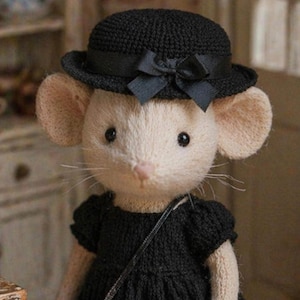 May include: A handcrafted plush mouse wearing a black dress, a matching hat with a bow, and a small purse. The mouse has a light beige body, large ears, and a pink nose. The outfit is knitted, giving it a textured appearance.