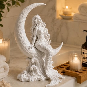 Puede incluir: Escultura de sirena blanca sentada en una luna creciente. La escultura tiene cabello largo y fluido y est&aacute; detallada con patrones de olas en la base. Decoraci&oacute;n adecuada para ba&ntilde;o o dormitorio.