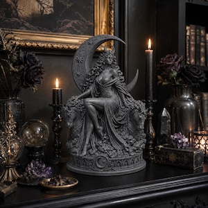 Puede incluir: Una escultura de resina gris oscuro de una figura sentada con cabello largo y fluido y un tocado de media luna, frente a un gran fondo de media luna. La figura se sienta entre dos cabezas de caballo sobre una base con un emblema de luna y estrella.