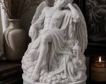 Puede incluir: Una escultura blanca de un ángel reclinado sobre una base en forma de nube. El ángel tiene alas detalladas y está cubierto de tela. Una pequeña linterna con una luna creciente y estrellas está colocada junto al ángel. La base tiene un diseño floral.