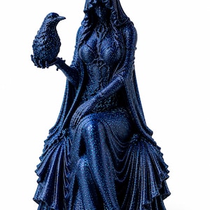 May include: A dark blue glittery figurine of a seated hooded figure wearing a long flowing gown with intricate bodice detailing. The figure holds a small bird perched on one hand, with the hood obscuring the face and the gown draped in folds.