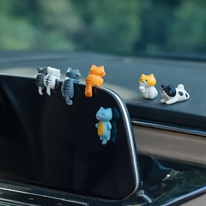 Puede incluir: Una colección de figuras de gatos coloridos en varias poses. Las figuras son en tonos de gris, naranja, blanco y azul. Algunas están posadas sobre una superficie negra, mientras que otras están de pie o tumbadas. El tema general es un diseño de gato lindo y juguetón.