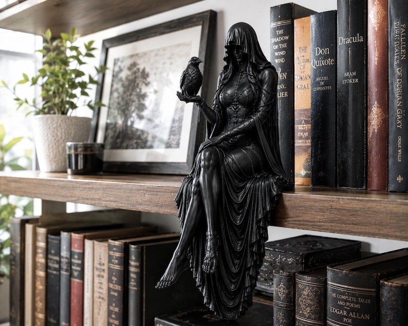 May include: A black figurine of a hooded figure sitting on a shelf edge, wearing a long flowing gown and holding a small bird in one hand. The figure has detailed textures on the bodice and skirt, with bare feet hanging down over the shelf edge.