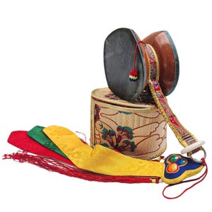 Puede incluir: Un tambor damaru tibetano tradicional con una caja cilíndrica y cintas de seda coloridas. El tambor tiene dos caras grises oscuras y un cuerpo de madera marrón. La caja es beige con motivos florales. Las cintas son rojas, verdes y amarillas.