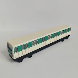 Può includere: Un modellino di vagone ferroviario con tetto color crema e fianchi verdi e bianchi. Il vagone ha ruote nere ed è progettato per assomigliare a una carrozza della metropolitana. Le finestre sono rettangolari.