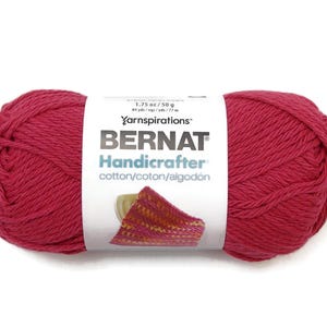 May include: A skein of Bernat Handicrafter cotton yarn in a vibrant red hue. The label indicates 1.75 oz (50 g) and 84 yards (77 m). The yarn is designed for crafting projects. The label also shows a knitted swatch.