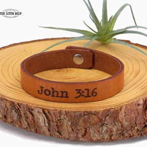 May include: Brown leather bracelet with the text "John 3:16" engraved on it.