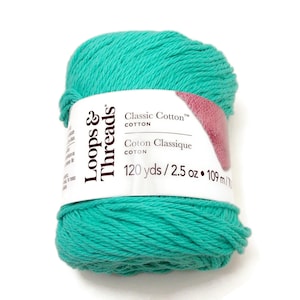 May include: A ball of teal-colored Loops & Threads Classic Cotton yarn. The label indicates 120 yards of yarn and 2.5 oz. The yarn is tightly wound, and the label has pink and white accents.