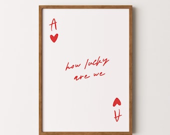 May include: A framed wall art print featuring a white background with red text and graphics resembling an ace of hearts playing card. The design includes the letter A, a heart symbol, and the handwritten red text that reads how lucky are we.