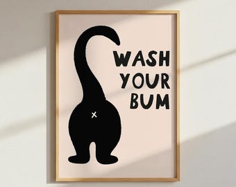 May include: A framed wall art print featuring a black silhouette of a cat from behind with its tail raised. The text WASH YOUR BUM is printed in bold black letters to the right of the cat. A small white cross marks the center of the silhouette.