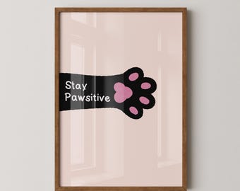 May include: A framed print featuring a black cat paw with pink paw pads. The paw extends from a black band with the words "Stay Pawsitive" in white. The background is a soft pink color.