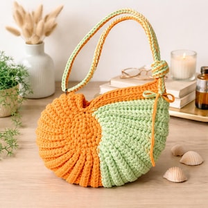May include: A handmade crochet handbag in orange and light green. The bag features a rounded shape with a knotted handle in matching colors. The bag is made of thick yarn and has a textured appearance. The bag is a unique accessory.