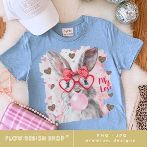 May include: A light blue t-shirt featuring a bunny wearing heart-shaped glasses and a bow, blowing a bubblegum bubble. The graphic includes the text "My Love" and leopard print hearts. A white baseball cap is visible.