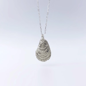 May include: A silver necklace with a detailed oyster shell pendant.