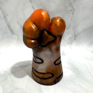 May include: A resin sculpture shaped like a stylized animal paw, featuring a marbled blend of orange, brown, and white tones. The design includes recessed black outlines that define the paw pads and toes, creating a smooth, glossy finish throughout.