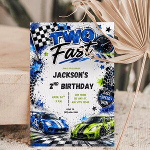 May include: A rectangular birthday invitation card featuring a blue and green race car theme with a checkered flag, speedometer, and tire tracks. The text reads TWO FAST, JACKSON'S 2ND BIRTHDAY, APRIL 24TH, 3 P.M., OUR HOME, 123 ANY ST., ANY CITY 12345, and RSVP TO (123)-456-7890.