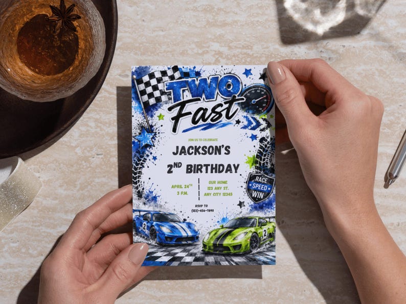 May include: A rectangular birthday invitation card featuring a race car theme with blue and green sports cars, a checkered flag, and tire tracks. The text reads TWO FAST, JACKSON'S 2ND BIRTHDAY, APRIL 24TH, 3 P.M., OUR HOME, 123 ANY ST., ANY CITY 12345, and RSVP TO (555)-555-7890.