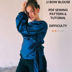 Op de afbeelding: Een diepblauwe satijnen overslagblouse met lange, geplooide mouwen en een striksluiting aan de zijkant. De tekst op de afbeelding luidt: JJ BOW BLOUSE, PDF SEWING PATTERN & TUTORIAL, DIFFICULTY, DoorsAndFloorsBlog.com, met twee oranje cirkels.