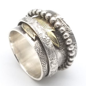 May include: A silver and gold spinning ring with a beaded edge and an engraved design. The ring has a textured surface and a gold leaf design.