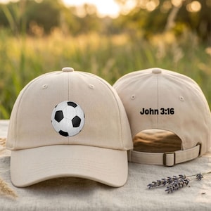 May include: Tan baseball cap with a soccer ball graphic on the front. The back of the cap has the text "John 3:16". The cap has an adjustable strap and a curved brim. The cap is made of a soft material.