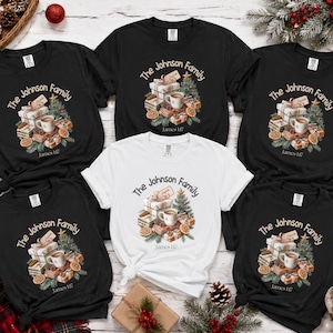 May include: A collection of five short-sleeve t-shirts, four black and one white, each featuring a graphic of a Christmas tree, wrapped gifts, a mug, and orange slices. The text reads The Johnson Family and James 1:17 in a circular design.