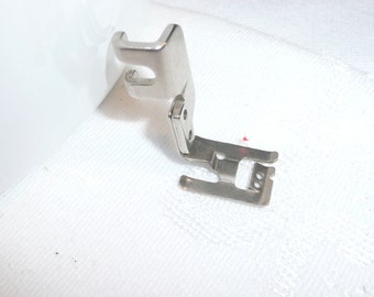 May include: A silver sewing machine foot with a metal attachment. The foot is designed for sewing straight seams.