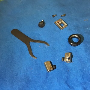 May include: A set of sewing machine parts including a foot, a needle plate, a screw, a wrench, and a black ring.