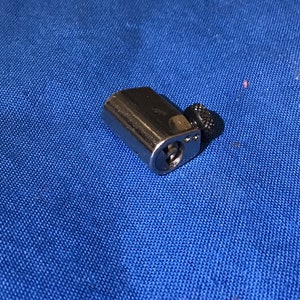 Może przedstawiać: Srebrny cylinder zamka z czarnym pokrętłem. Cylinder ma dziurkę od klucza i mały metalowy kołek.