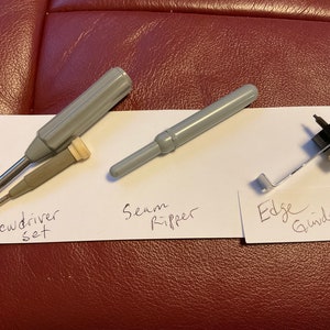 Peut inclure: Un ensemble de trois outils de couture&nbsp;: un jeu de tournevis, un d&eacute;couseur et un guide de bord. Les outils sont dispos&eacute;s sur une surface blanche avec des &eacute;tiquettes manuscrites.
