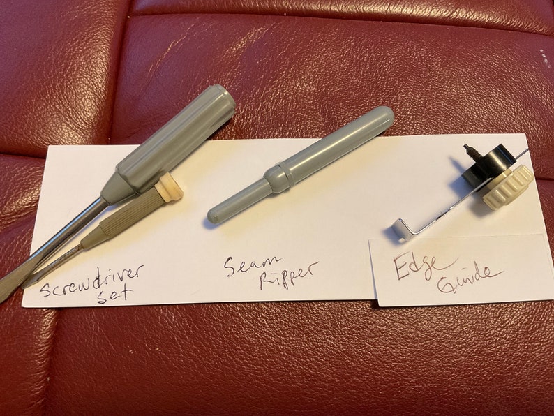 Peut inclure: Un ensemble de trois outils de couture&nbsp;: un jeu de tournevis, un d&eacute;couseur et un guide de bord. Les outils sont dispos&eacute;s sur une surface blanche avec des &eacute;tiquettes manuscrites.