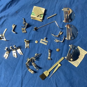 Peut inclure: Un ensemble de pieds de machine &agrave; coudre et d'accessoires, comprenant une brosse, un tournevis et une aiguille. Les pieds sont en m&eacute;tal et ont diff&eacute;rentes formes et tailles. Les accessoires sont &eacute;galement en m&eacute;tal et sont utilis&eacute;s pour diff&eacute;rentes t&acirc;ches de couture.