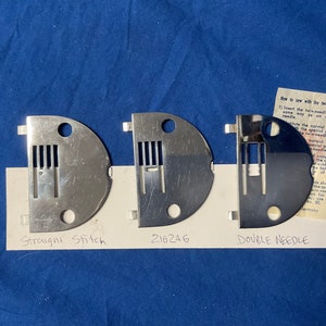 Peut inclure: Trois plaques &agrave; aiguilles en m&eacute;tal pour machine &agrave; coudre, &eacute;tiquet&eacute;es "Point droit", "216246" et "Double aiguille".